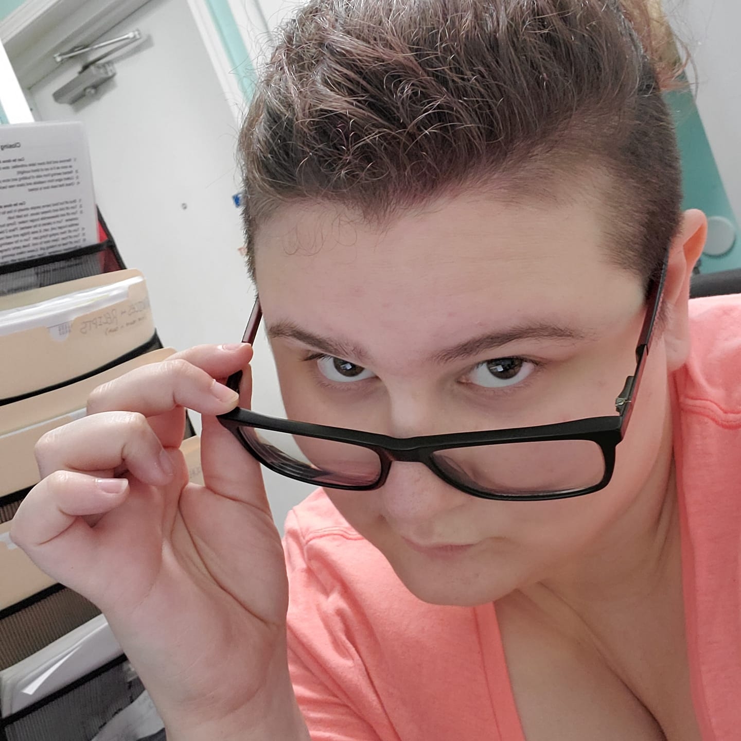 A person holding their glasses low on their nose and looking up at the camera.